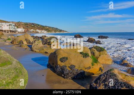 Große felsige Küste von Malibu Beach mit Häusern im Hintergrund vor einem klaren Himmel. Stockfoto
