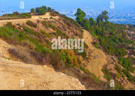 Panoramablick auf die Wanderwege im Griffith Park, auf denen sich Wanderer auf gewundenen Pfaden mit einer Stadtlandschaft in der Ferne unter klarem Himmel bewegen. Stockfoto