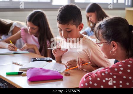 Grundschullehrerin, die einem ihrer Schüler während des Unterrichts in einem Klassenzimmer hilft. Stockfoto