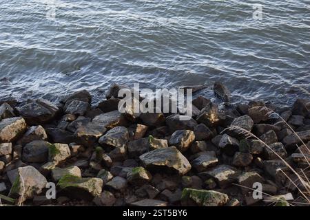 Wasserkräuseln, die über moosige Felsen an einer felsigen Küste gespült werden, aus nächster Nähe. Stockfoto