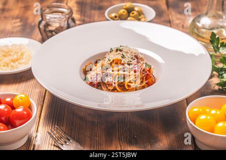 Spaghetti- oder Puttanesca-Pasta nach traditionellem italienischem Rezept mit Sardellen, Oliven, Kapern auf einer weißen Platte auf einem hölzernen Hintergrund mit in Stockfoto
