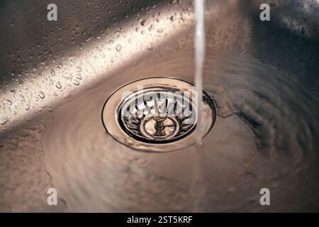 Wasser im neuen Abfluss aus metallischem Spülbecken, selektiver Fokus Stockfoto