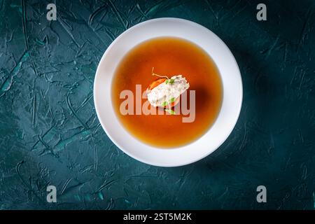 Suppe oder Consomme, dicke Fleischbrühe mit Karotten, Hühnerknödel und Mikrogrün, serviert auf einem weißen Teller auf dunkelgrünem Hintergrund. Blick aus der ganzen Welt Stockfoto