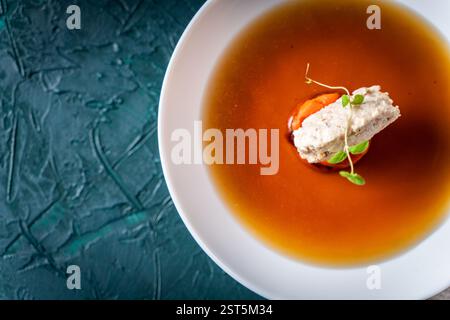 Suppe oder Consomme, dicke Fleischbrühe mit Karotten, Hühnerknödel und Mikrogrün, serviert auf einem weißen Teller auf dunkelgrünem Hintergrund. Blick aus der ganzen Welt Stockfoto
