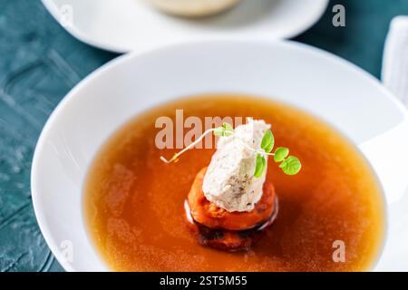 Suppe oder Consomme, dicke Fleischbrühe mit Karotten, Hähnchenknödel serviert auf einem weißen Teller auf dunkelgrünem Hintergrund mit Sesambrötchen, Serviette und Stockfoto