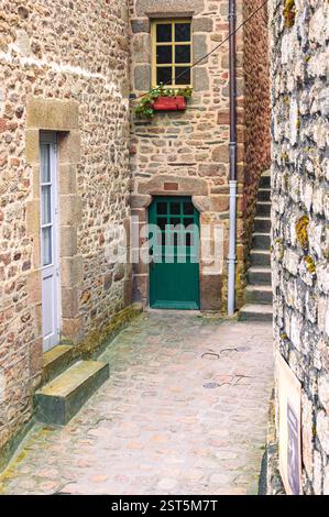 Mont Saint-Michel, Frankreich - 25. Januar 2016: Eine charmante, enge Gasse mit Steinmauern, einer grünen Tür und einer Treppe, die nach oben führt. Stockfoto