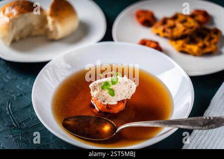 Suppe oder Consomme, dicke Fleischbrühe mit Karotten, Hühnerknödel serviert auf einem weißen Teller auf dunkelgrünem Hintergrund mit Löffel. Blick von oben. Spa Stockfoto