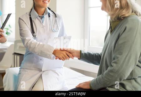 Freundlicher Arzt schüttelt die Hände mit älteren Patienten, die in der medizinischen Klinik sitzen Stockfoto