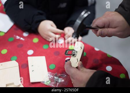 Der Mann hämmert ein Stück Holz. Ein Kind beobachtet ihn. Der Tisch ist rot und hat Polka Dots Stockfoto