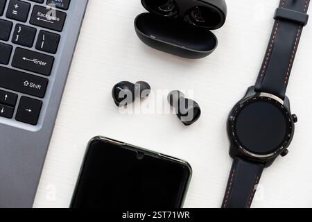 Ein Laptop, eine Smart Watch, Kopfhörer und ein Smartphone auf einem Holztisch. Stockfoto