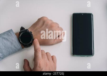 Ein Mann hält ein Smartphone und eine Smartwatch in der Hand. Kabellose Verbindung von Uhr und Mobiltelefon. Wi-Fi-Anschluss für Smartphone und Smartwatch Stockfoto