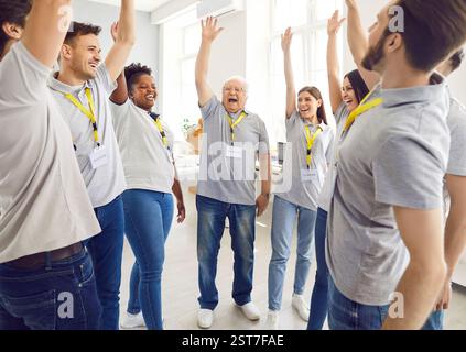 Freiwillige stehen im Kreis und halten die Hände hoch und lächeln, arbeiten im gemeinnützigen Wohltätigkeitszentrum. Stockfoto
