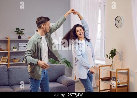 Fröhliches, lachendes junges Paar, das zu Hause im Wohnzimmer tanzt. Stockfoto