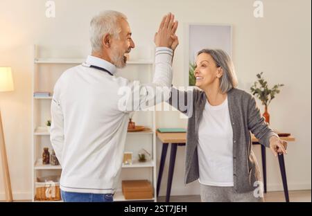 Seniorenpaar, die einander hohe fünf geben, freuen sich über Erfolg im Wohnzimmer zu Hause zu stehen. Stockfoto