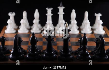 Nahaufnahme. Schwarze Schachfiguren gegenüber weißen, entlang des Bretts. Auf isoliertem schwarzem Hintergrund Stockfoto