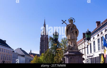 Die Statue des Heiligen Johannes von Nepomuk vor der Kirche unserer Lieben Frau in Brügge unter einem sonnigen Himmel. Ikonische Mischung aus glaube, Geschichte und europäischer Architektur. Stockfoto