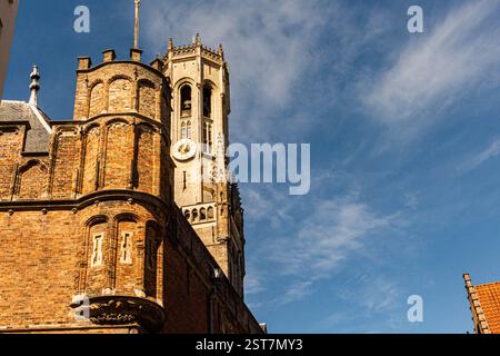 Der Glockenturm von Brügge ragt über einem alten Dach, eingerahmt von einem blauen Himmel mit weißen Wolken an einem sonnigen Septembertag. Stockfoto