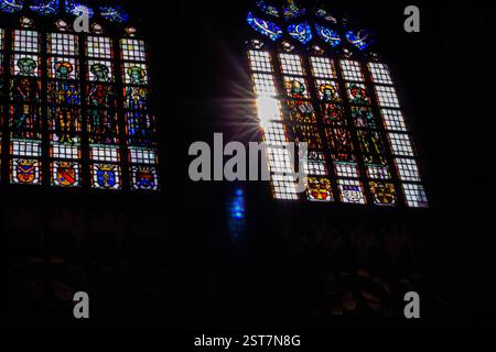 Das Buntglasfenster leuchtet in einer dunklen Kirche, mit Sonnenstrahlen, die bunte Reflektionen erzeugen und heilige Kunst und Licht in einem ruhigen Inneren verschmelzen. Stockfoto