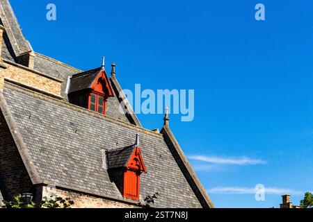 Brügge-Dach mit roten Fenstern steht im Kontrast zum tiefblauen Sommerhimmel und bietet lebhafte Farben und historische europäische Architektur. Stockfoto