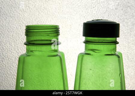 Zwei Wasserflaschen aus grünem Kunststoff, von denen eine einen Verschluss gegen strukturiertes Glas hat Stockfoto