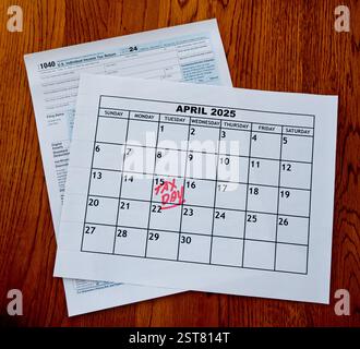 April 2025 Kalender mit Steuertag - 15. April - in roten handgeschriebenen Briefen und IRS Form 1040 sitzend auf Holztisch Stockfoto