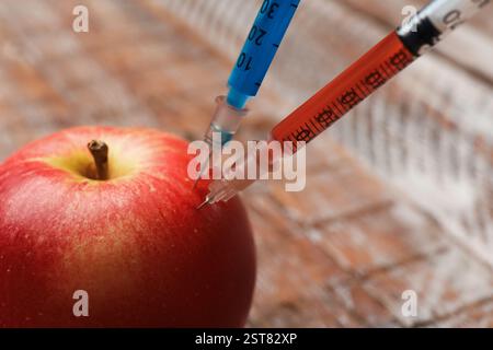 GVO-Konzept. Roter Apfel mit Spritzen auf verschwommenem Hintergrund, Nahaufnahme Stockfoto