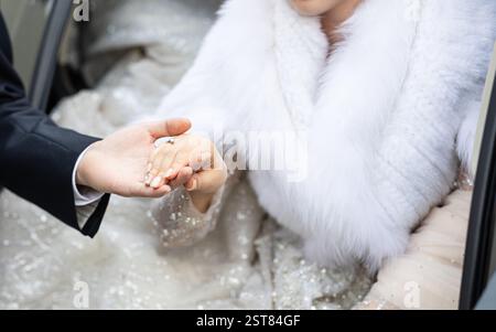 Ein Mann und eine Frau halten die Hände. Die Frau trägt einen weißen Pelzmantel. Der Mann trägt einen schwarzen Anzug Stockfoto
