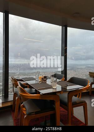 Dieses atemberaubende Foto zeigt ein Hochhausrestaurant mit raumhohen Fenstern, die einen atemberaubenden Panoramablick auf die Skyline der Stadt bieten, einschließlich Stockfoto