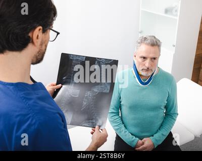 Älterer Mann mit Nackenverletzung in einer Halsbandage während der Beratung mit einem Handtherapeuten, der sich eine MRT des Nackens des Patienten anschaut Stockfoto