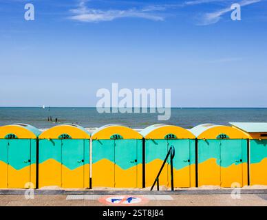 Eine Reihe bezaubernder, verwitterter gelb-grüner Strandhütten mit grafischem Muster, die Geschichten von unzähligen europäischen Sommern am Ufer erzählen. Stockfoto