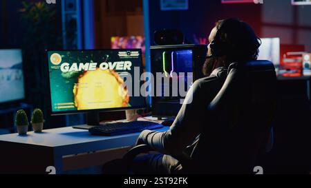 Ein verärgerter Gamer trifft frustriert auf den Schreibtisch, nachdem er ein Spiel über den Bildschirm erhalten hatte und sein Raumschiff im Flugspiel zerstört wurde. Trauriger Spieler, der enttäuscht ist, nachdem er Science-Fiction-Videospiel verloren hat Stockfoto