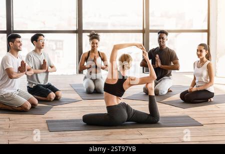 Flexibler Yoga-Coach Für Frauen, Der Menschen Beim Gruppentraining Asana-Übungen Zeigt Stockfoto