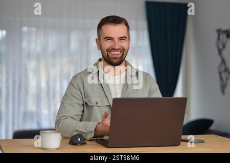 Ein glücklicher Mann, der einen Laptop benutzt, während er im Heimbüro arbeitet. Stockfoto