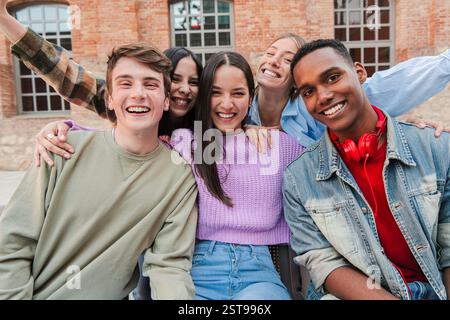 Fröhliche Gruppe von fünf jungen Freunden, die hell lächeln, während sie gemeinsam für ein lustiges Foto posieren und ihr Glück und ihre Verbindung in einer lebhaften Zusammenkunft voller Lachen und Aufregung zeigen. Hochwertige Fotos Stockfoto