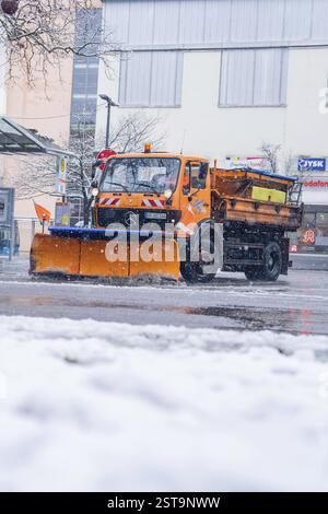 Orangefarbener Schneepflug auf einer schneebedeckten Straße in einer städtischen Umgebung, Sindelfingen, Deutschland, Europa Stockfoto