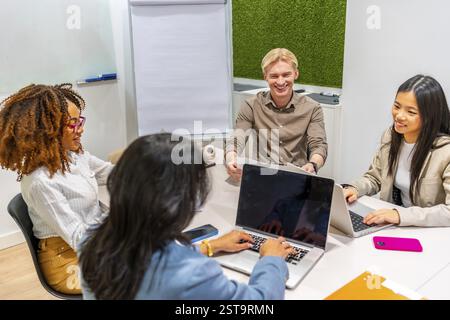 Kollegen aus verschiedenen Ethnien, die Laptops nutzen und während eines produktiven Meetings in einem Coworking-Raum diskutieren Stockfoto
