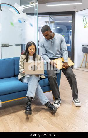 Zwei junge Profis arbeiten zusammen, tauschen Ideen aus und nutzen einen Laptop in einem modernen Coworking-Büro Stockfoto