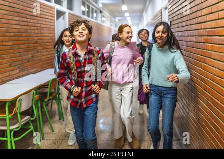 Fröhliche Schüler mit Rucksäcken, die durch den Schulflur rasen, ihre Pause zwischen den Klassen genießen und fröhliche Momente miteinander teilen Stockfoto