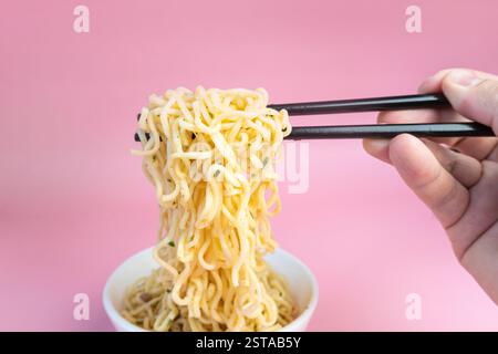 Männliche Hand rührt Instant-Nudeln mit Stäbchen in einer Schüssel auf rosa Hintergrund. Stockfoto