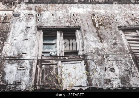 Veraltetes Gebäude mit schmutzigen Wänden und kaputten Fenstern in Stone Town, Sansibar. Verwitterte Fassade eines verlassenen Hauses. Äußere eines ruinösen Gebäudes. Stockfoto