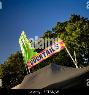Abgewinkelter Schuss eines Cocktail-Stände-Schildes und einer hellgrünen Festivalflagge vor einem klaren blauen Himmel Stockfoto