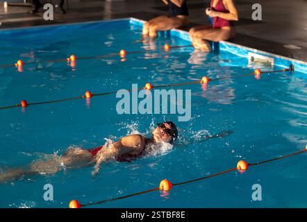 Schwimmer üben in einem Hallenbad und zeigen ihre Fähigkeiten, während sie während eines Trainings durch das Wasser gleiten. Helles Licht hebt ihre Bewegung hervor Stockfoto