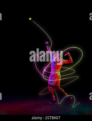 Fokussierter Mann, Tennisspieler in Bewegung, Servierball mit Schläger mit neongrünen und rosa Lichtspuren, die Bewegung vor schwarzem Hintergrund betonen. Stockfoto