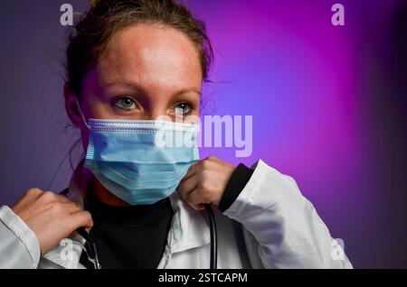 Arzt mit Schutzmaske und Stethoskop auf violettem Hintergrund Stockfoto