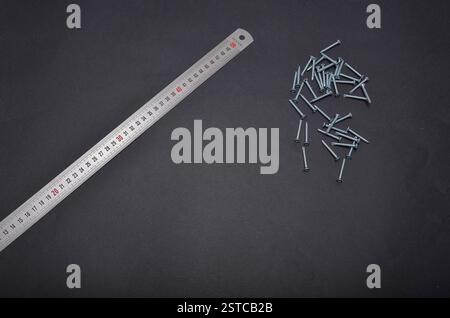 Metalllineal und Schrauben auf dunklem Hintergrund, bereit für Bau- und heimwerkerprojekte Stockfoto