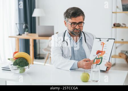 Der Mann zeigt eine Illustration. Konzeption der Diät. Professionelle medizinische Fachkraft in weißem Mantel ist im Büro. Stockfoto