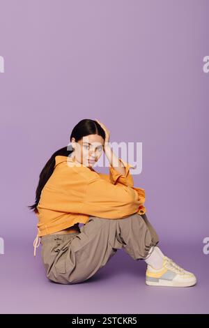 Eine stilvolle junge Frau sitzt anmutig und präsentiert ihr trendiges Outfit in einem hellen Ambiente. Stockfoto