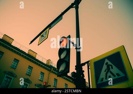 An einem Sommerabend heben sich die Fußgängerschilder und die rote Ampel vor der Kulisse der Skyline und der Gebäude hervor. Die Stadt ist Stockfoto