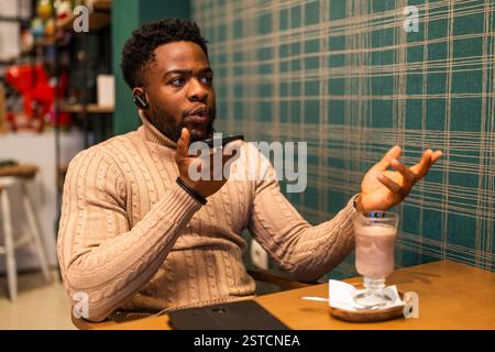 Der junge Mann hat eine Pause von der Arbeit, er spricht auf dem Smartphone und trinkt heiße Schokolade in der Bar. Stockfoto