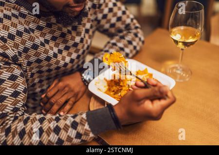 Nahaufnahme eines jungen schwarzen Mannes, der im Restaurant zu Abend essen und Wein trinkt. Stockfoto